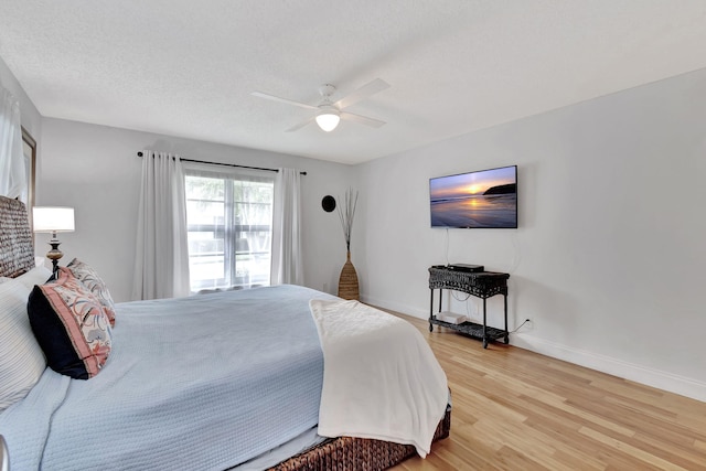 bedroom featuring light wood finished floors, a textured ceiling, baseboards, and a ceiling fan