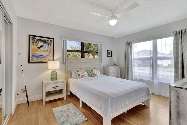 bedroom with a textured ceiling, multiple windows, light wood-style flooring, and baseboards