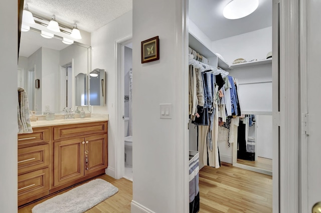 bathroom featuring a textured ceiling, toilet, wood finished floors, vanity, and a walk in closet