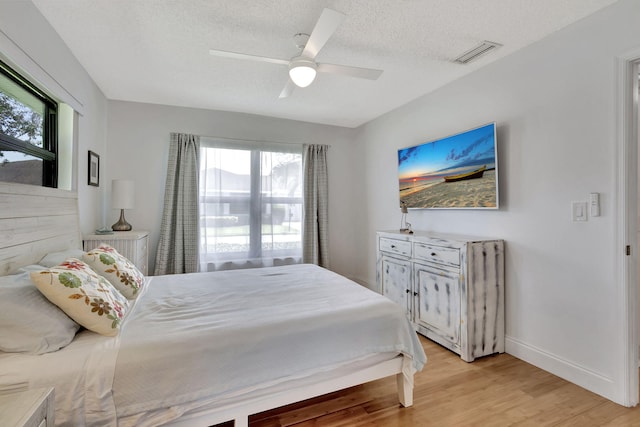 bedroom featuring a textured ceiling, a ceiling fan, baseboards, visible vents, and light wood-style floors