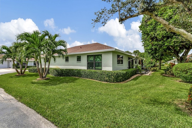 view of side of home featuring concrete driveway, roof with shingles, a lawn, and stucco siding