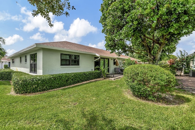 view of front facade with a patio, roof with shingles, a front yard, and stucco siding