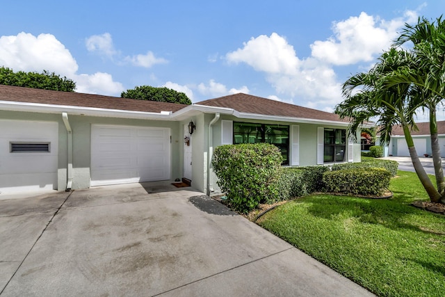 ranch-style home featuring concrete driveway, a front yard, an attached garage, and stucco siding