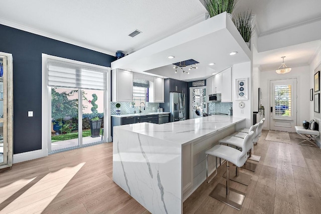 kitchen featuring light stone counters, a peninsula, decorative backsplash, light wood-style floors, and appliances with stainless steel finishes