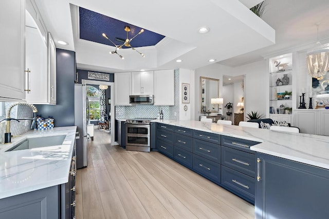 kitchen featuring an inviting chandelier, a sink, stainless steel appliances, white cabinets, and a raised ceiling