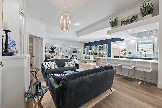 living area featuring light wood-type flooring, a notable chandelier, a tray ceiling, recessed lighting, and crown molding