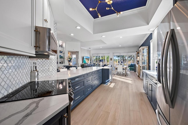 kitchen featuring light stone counters, stainless steel fridge, a raised ceiling, and light wood finished floors