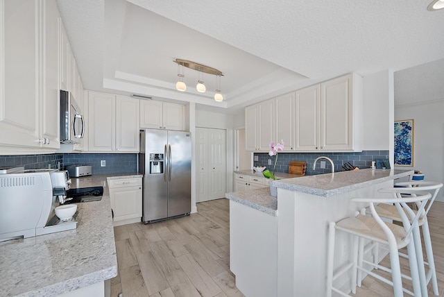 kitchen with appliances with stainless steel finishes, a tray ceiling, light wood-style flooring, and a peninsula