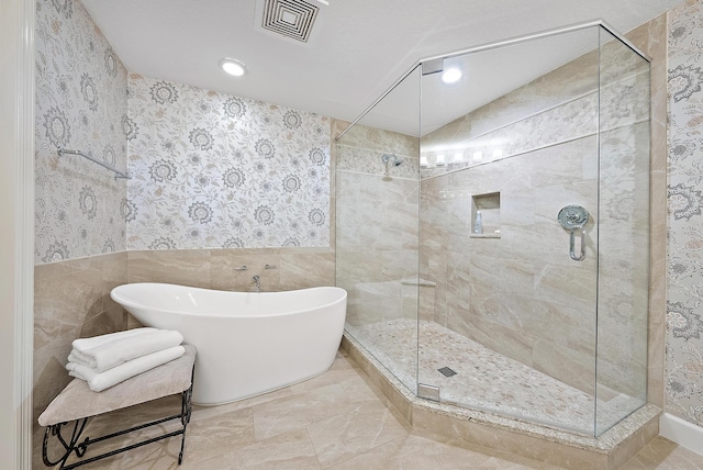 bathroom featuring a stall shower, a freestanding tub, visible vents, and wallpapered walls