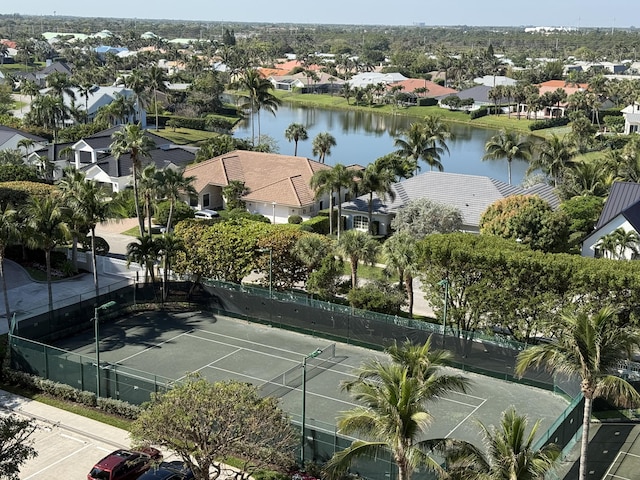 view of tennis court featuring a residential view, a water view, and fence