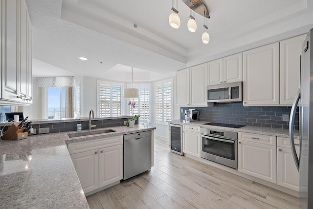 kitchen with tasteful backsplash, a raised ceiling, wine cooler, appliances with stainless steel finishes, and a sink