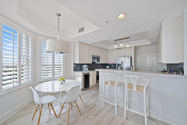 kitchen with wine cooler, a peninsula, appliances with stainless steel finishes, decorative backsplash, and a raised ceiling