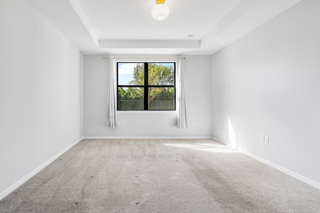 carpeted spare room with a tray ceiling and baseboards