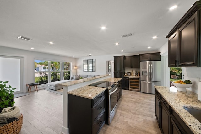 kitchen featuring open floor plan, light stone counters, appliances with stainless steel finishes, and visible vents