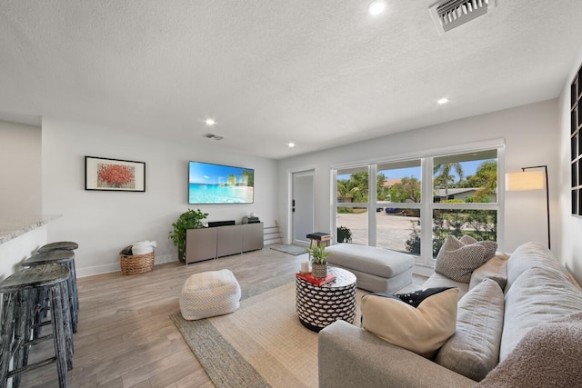 living room featuring a textured ceiling, visible vents, wood finished floors, and recessed lighting