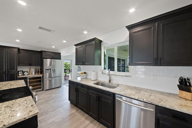 kitchen featuring light wood finished floors, stainless steel appliances, visible vents, backsplash, and a sink