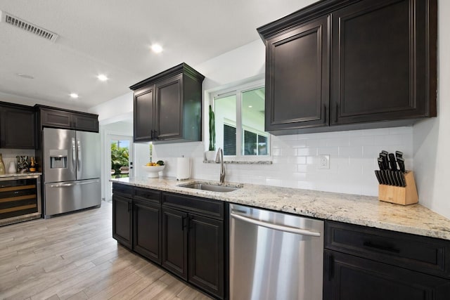 kitchen with light wood-style flooring, beverage cooler, stainless steel appliances, a sink, and visible vents