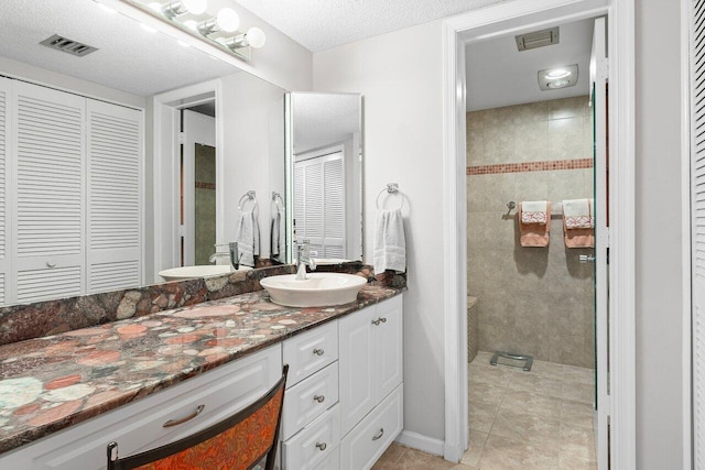 bathroom with visible vents, tile patterned flooring, a tile shower, vanity, and a closet