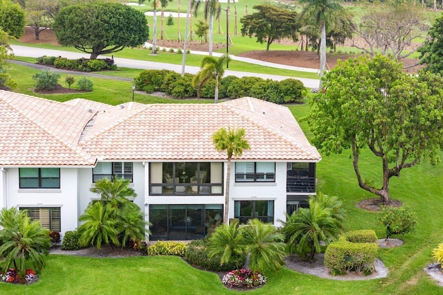 back of house featuring a tile roof, a lawn, and stucco siding