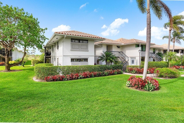 mediterranean / spanish house with a tile roof, stairs, a front lawn, and stucco siding