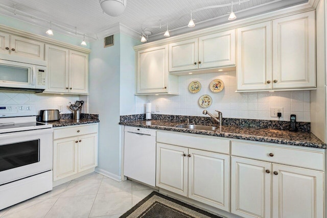 kitchen with light tile patterned floors, decorative backsplash, a sink, dark stone countertops, and white appliances