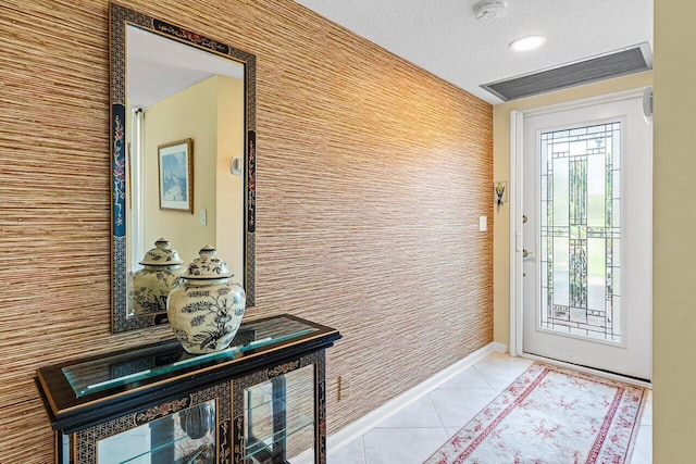 foyer with light tile patterned floors, wallpapered walls, baseboards, visible vents, and a textured ceiling