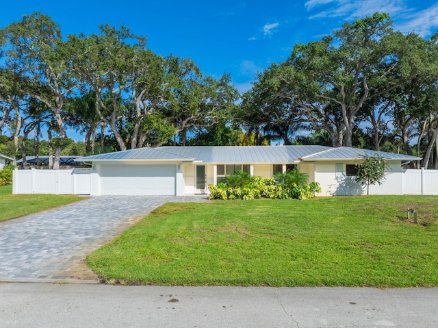 single story home featuring an attached garage, a standing seam roof, a front lawn, and decorative driveway