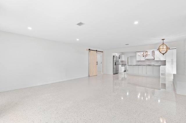 unfurnished living room with light speckled floor, a chandelier, a barn door, visible vents, and baseboards