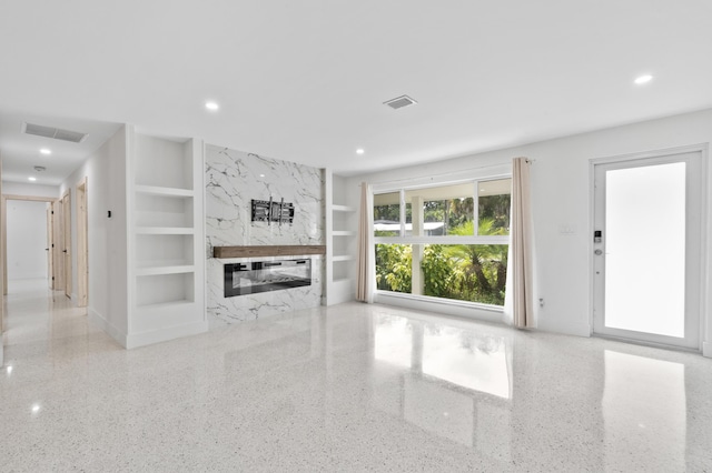 unfurnished living room featuring speckled floor, built in shelves, a fireplace, and visible vents