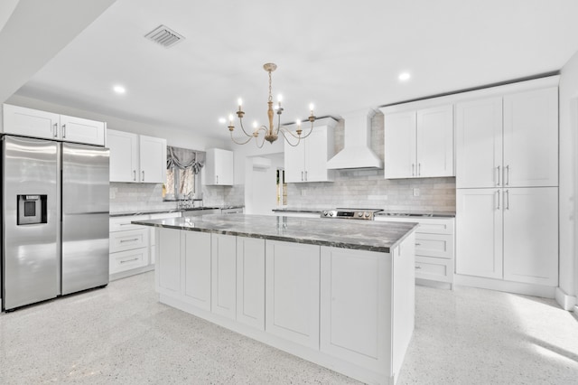 kitchen featuring visible vents, white cabinets, stainless steel fridge, and wall chimney range hood