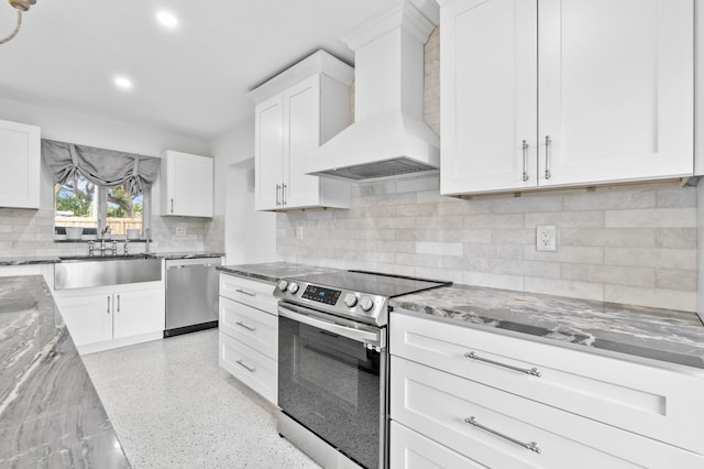 kitchen with custom exhaust hood, appliances with stainless steel finishes, white cabinets, a sink, and light stone countertops