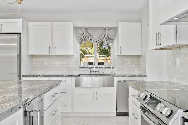 kitchen with wall chimney exhaust hood, light stone counters, stainless steel appliances, light speckled floor, and a sink