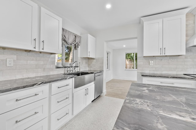 kitchen featuring decorative backsplash, white cabinets, dishwasher, dark stone countertops, and a sink