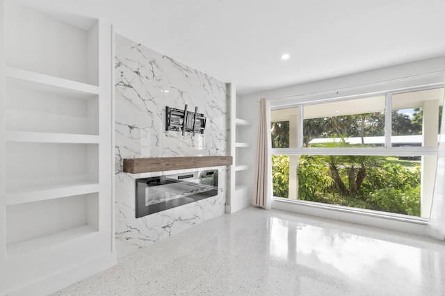 unfurnished living room featuring built in features, recessed lighting, a premium fireplace, and speckled floor