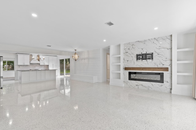 unfurnished living room with built in shelves, light speckled floor, visible vents, a high end fireplace, and a chandelier