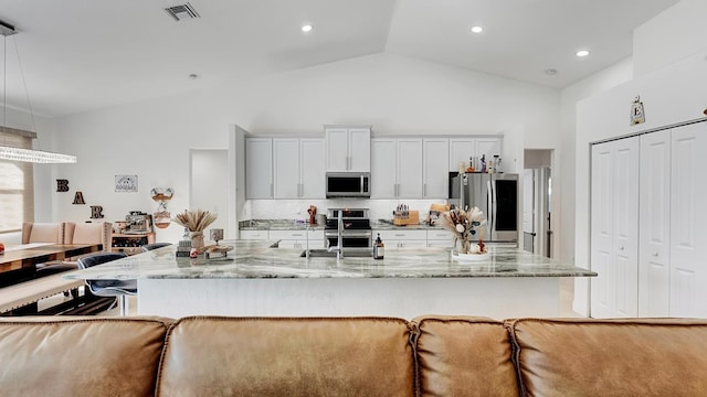 kitchen with visible vents, decorative backsplash, light stone countertops, stainless steel appliances, and a kitchen bar