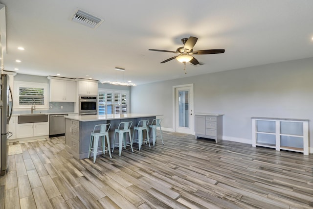 kitchen with visible vents, a kitchen island, stainless steel appliances, light wood-type flooring, and a sink