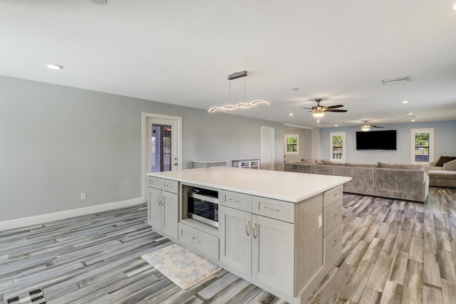 kitchen featuring light wood-style floors, stainless steel microwave, light countertops, and a center island