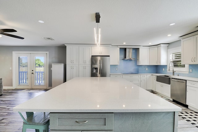 kitchen featuring stainless steel appliances, a sink, visible vents, wall chimney range hood, and a center island