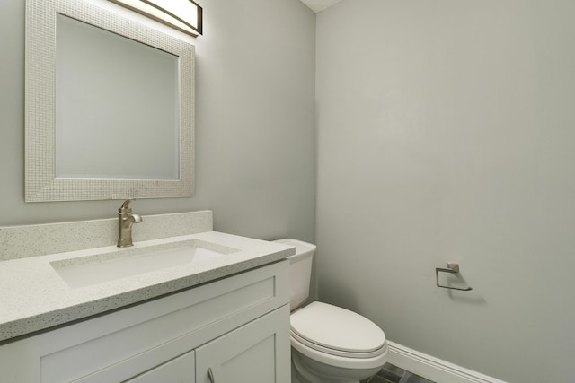 half bath featuring toilet, baseboards, and vanity