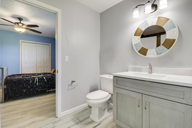 bathroom with toilet, a ceiling fan, vanity, wood finished floors, and baseboards