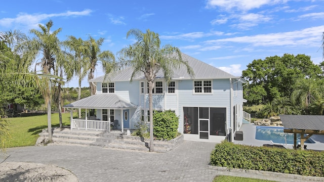 view of front facade with metal roof, a porch, a sunroom, decorative driveway, and a front lawn