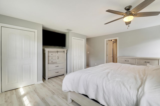 bedroom featuring light wood finished floors, visible vents, baseboards, a ceiling fan, and two closets