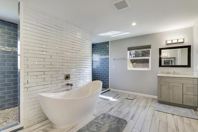 full bath with wood finish floors, vanity, tile walls, a freestanding bath, and tiled shower