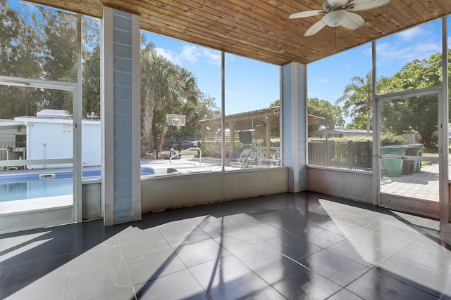 unfurnished sunroom with a healthy amount of sunlight, wood ceiling, and a ceiling fan