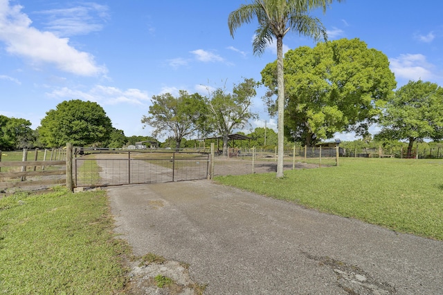 view of gate featuring a rural view, a lawn, and fence