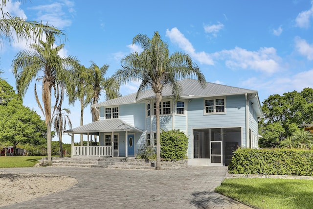 view of front facade featuring a sunroom, metal roof, covered porch, and decorative driveway