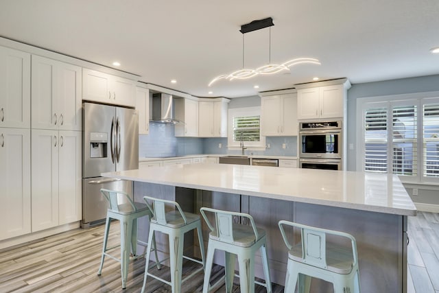 kitchen featuring light wood-style flooring, stainless steel appliances, white cabinets, wall chimney range hood, and tasteful backsplash