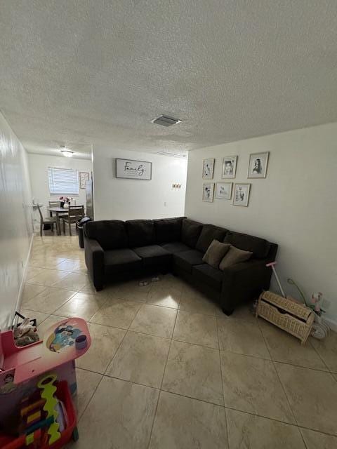 living area featuring visible vents, a textured ceiling, and light tile patterned flooring