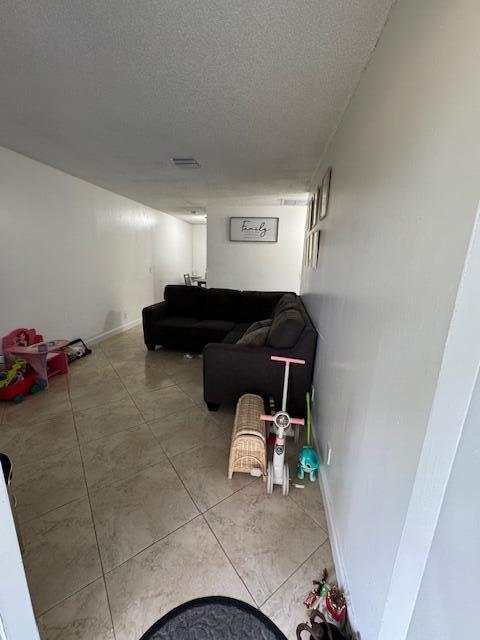 living room featuring baseboards, visible vents, a textured ceiling, and light tile patterned flooring